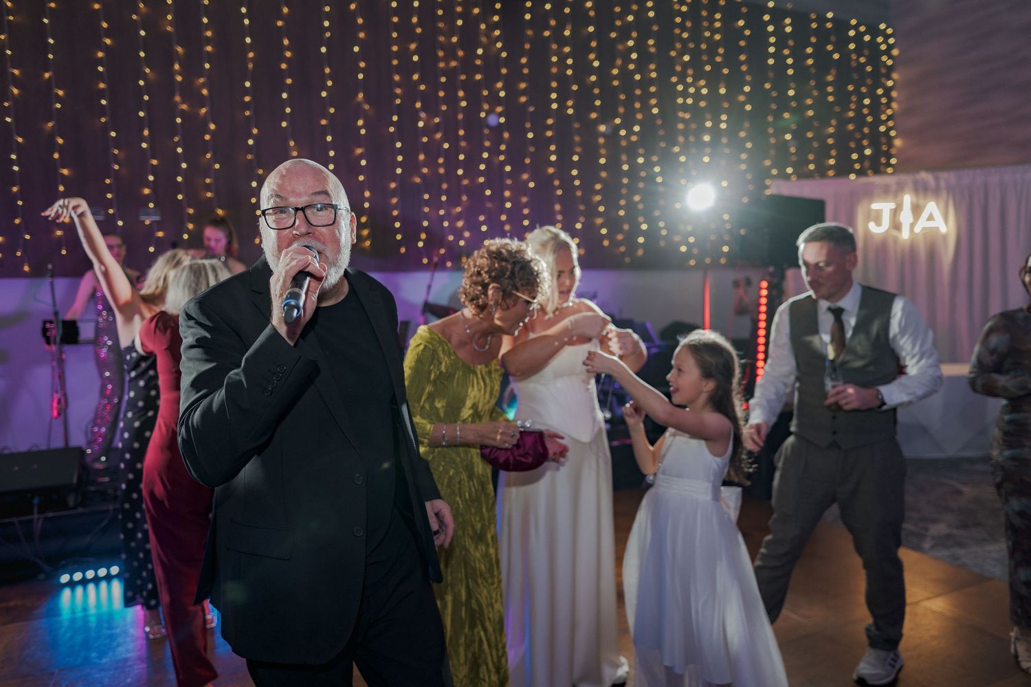 Wedding guests dancing together on a dimly lit dance floor with string lights glowing in the background.