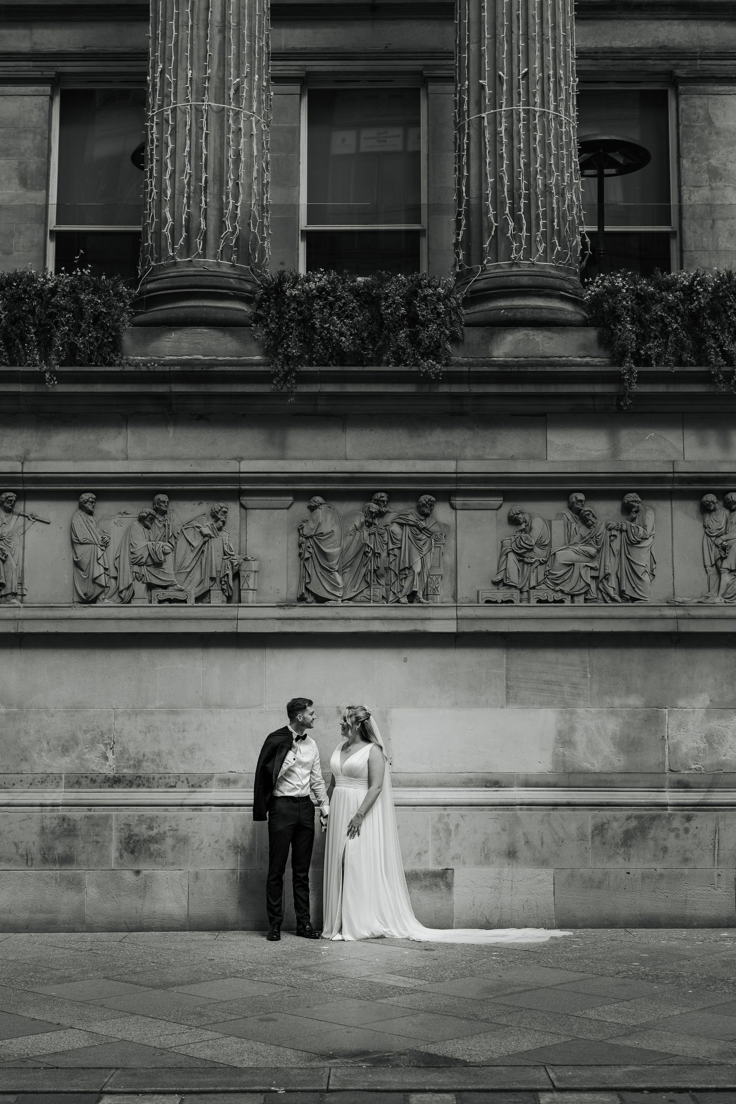 A black and white wedding photograph series showing a couple against a grand stone building with classical architecture.