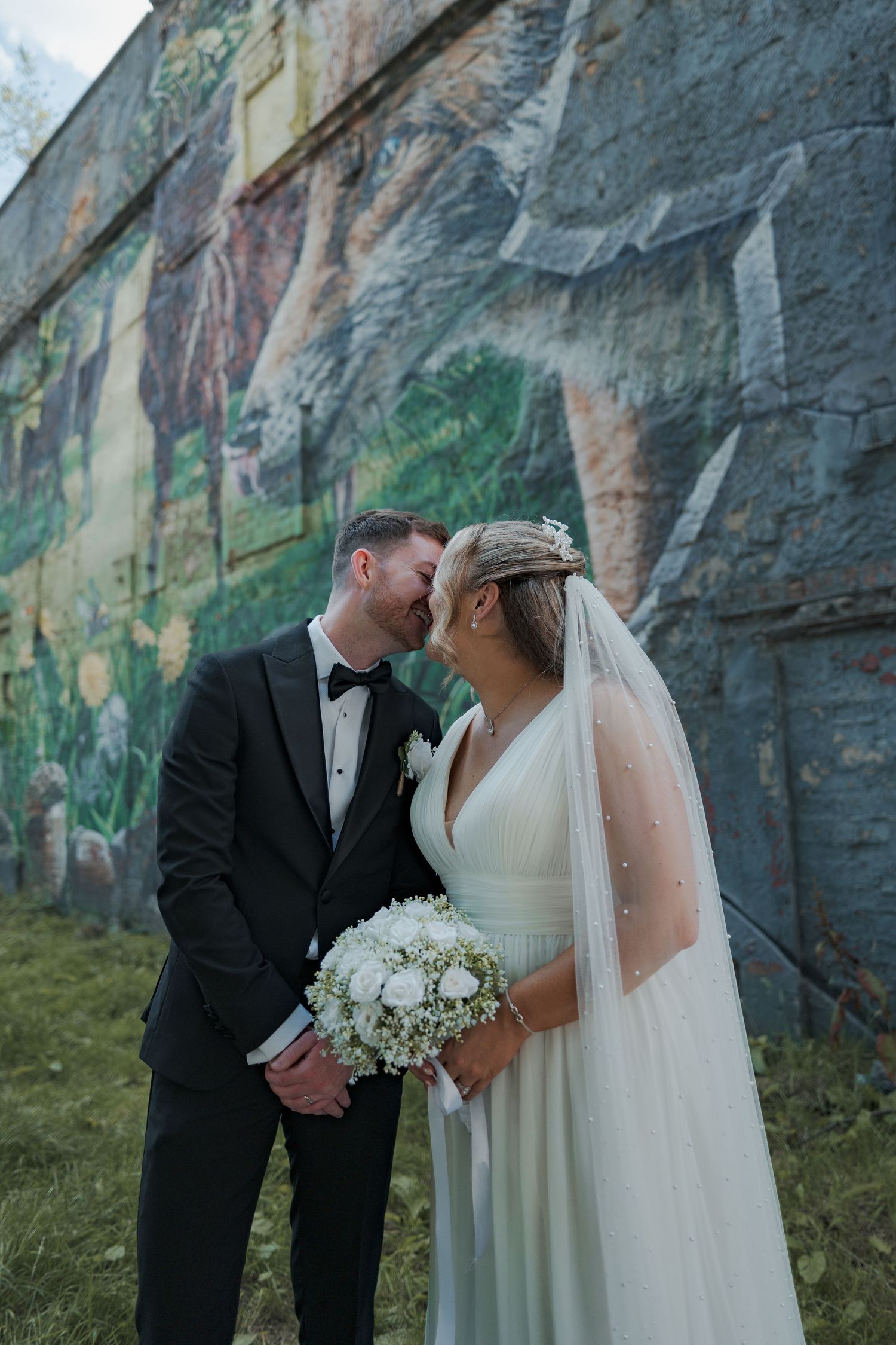 A couple in wedding attire pose for romantic photos against a dramatic rocky cliff backdrop.