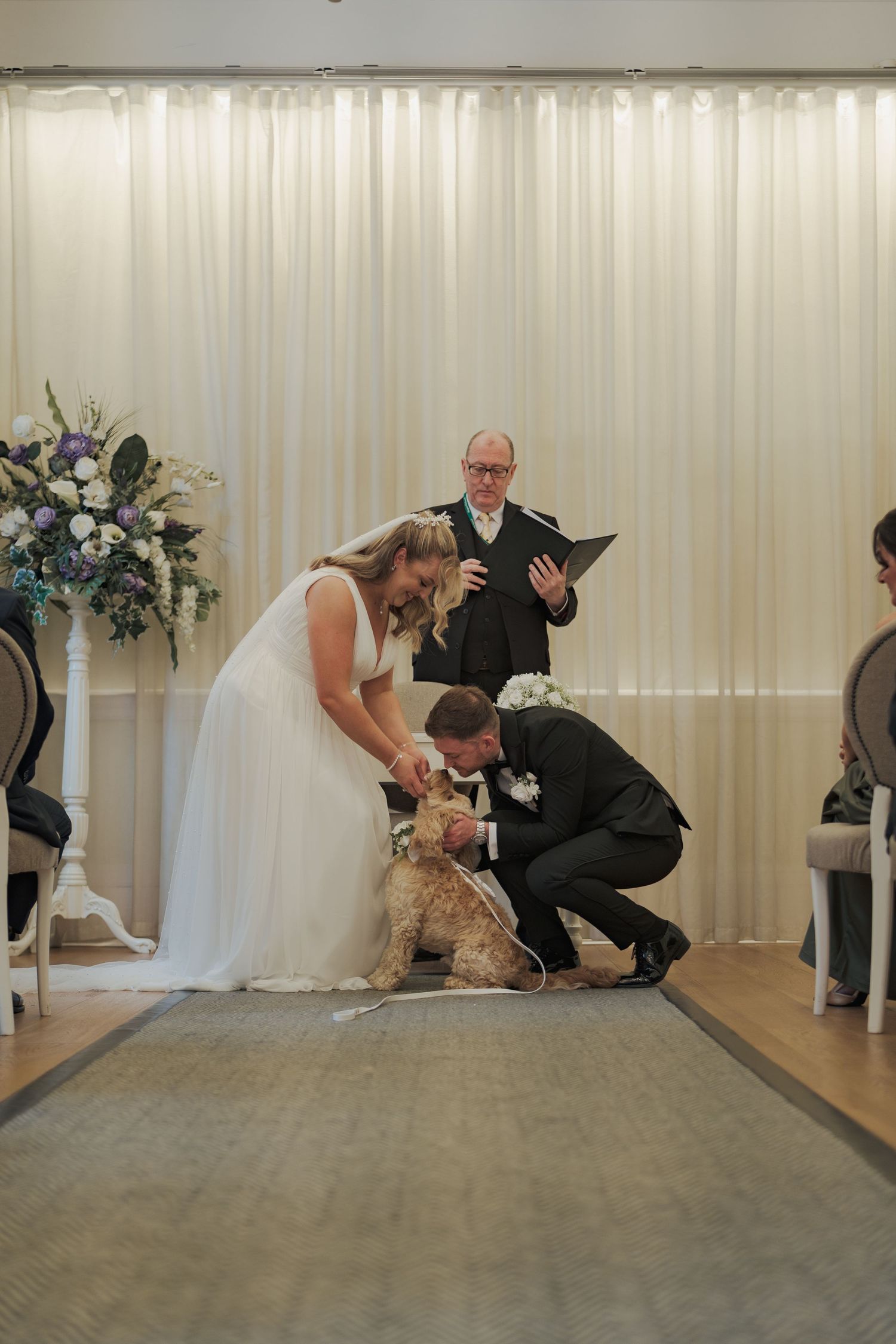 A couple at their wedding ceremony pauses to pet their dog while an officiant stands behind them with a book at 23 Montrose Street.