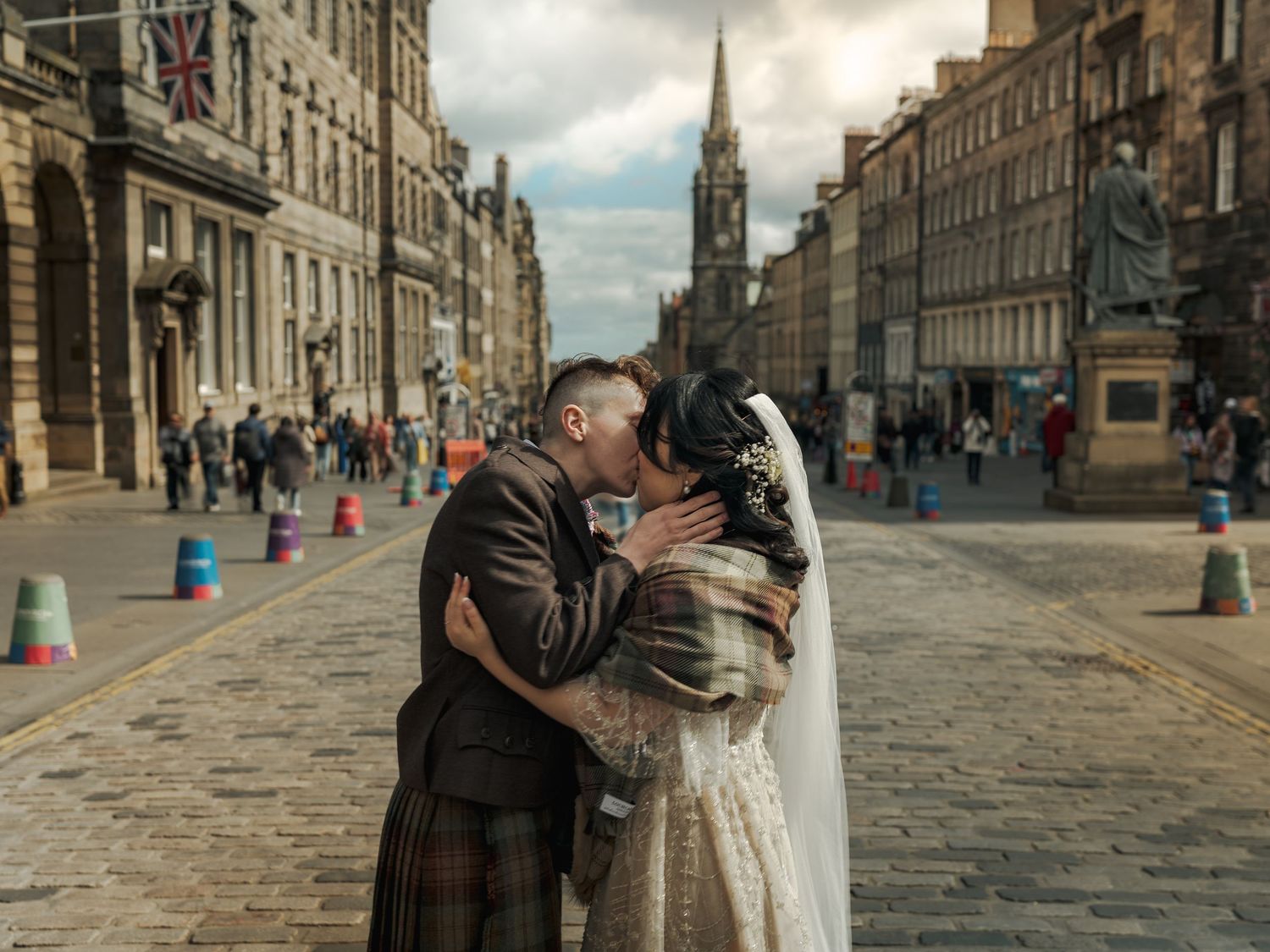 Newlywed couple kissing on the Royal Mile in Edinburgh, bride in white gown and groom in traditional Scottish kilt on the Royal Mile