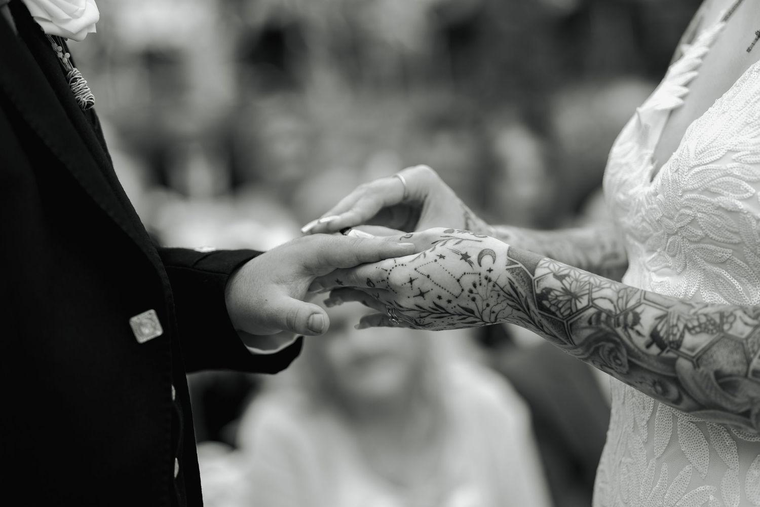 Black and white photo of a tattooed bride placing a wedding ring on the groom's finger during the ceremony.