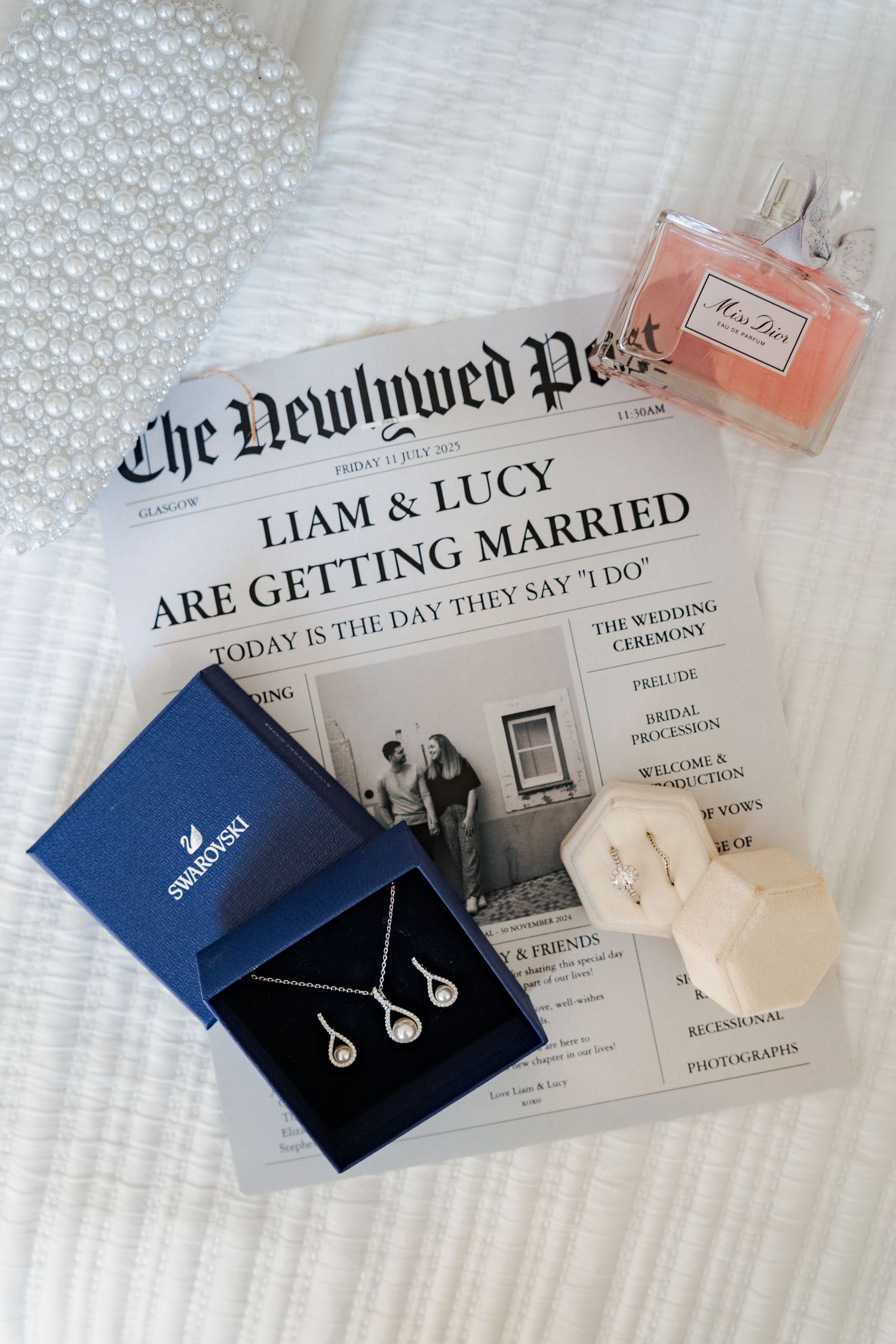 A series of navy blue jewelry boxes and wedding invitations arranged on white textured fabric with perfume bottles.