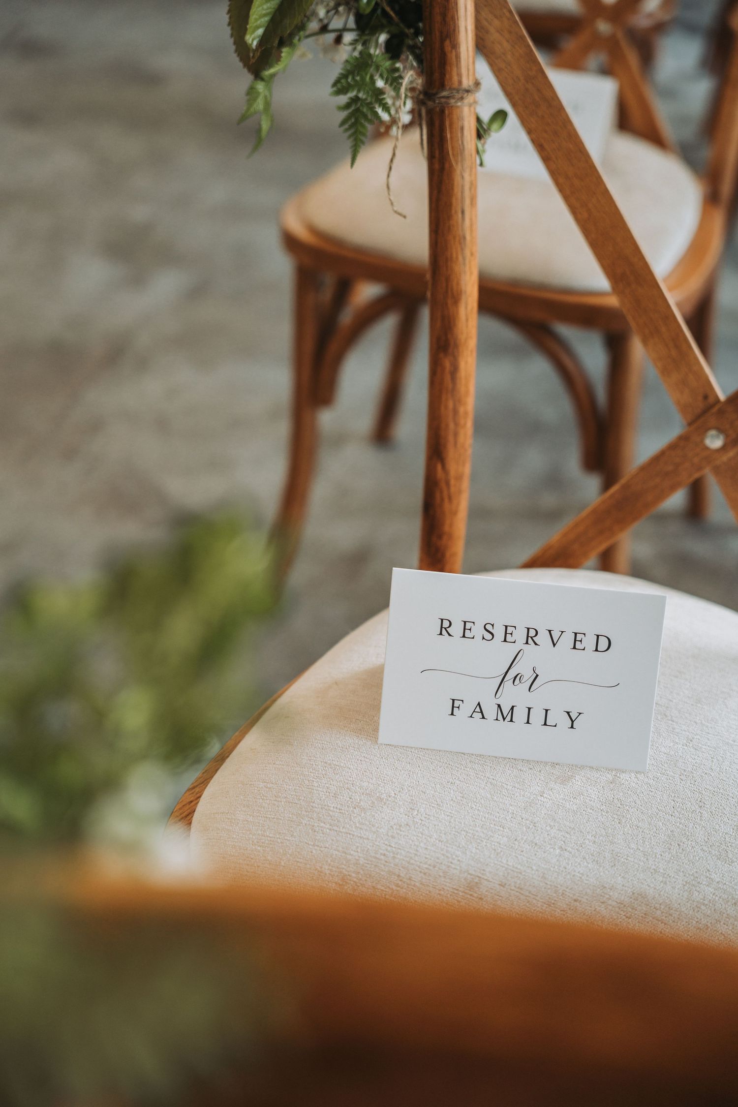 A 'Reserved for Family' sign placed on a wooden chair at an elegant event setting with green foliage details.