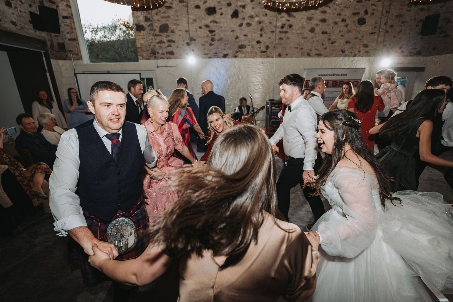 Party guests dancing energetically on a dance floor inside a rustic stone-walled venue during a celebration at Kinclune House