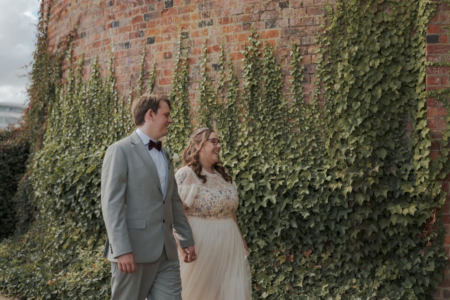 A couple shares romantic moments against an ivy-covered brick wall backdrop in an outdoor wedding photoshoot.