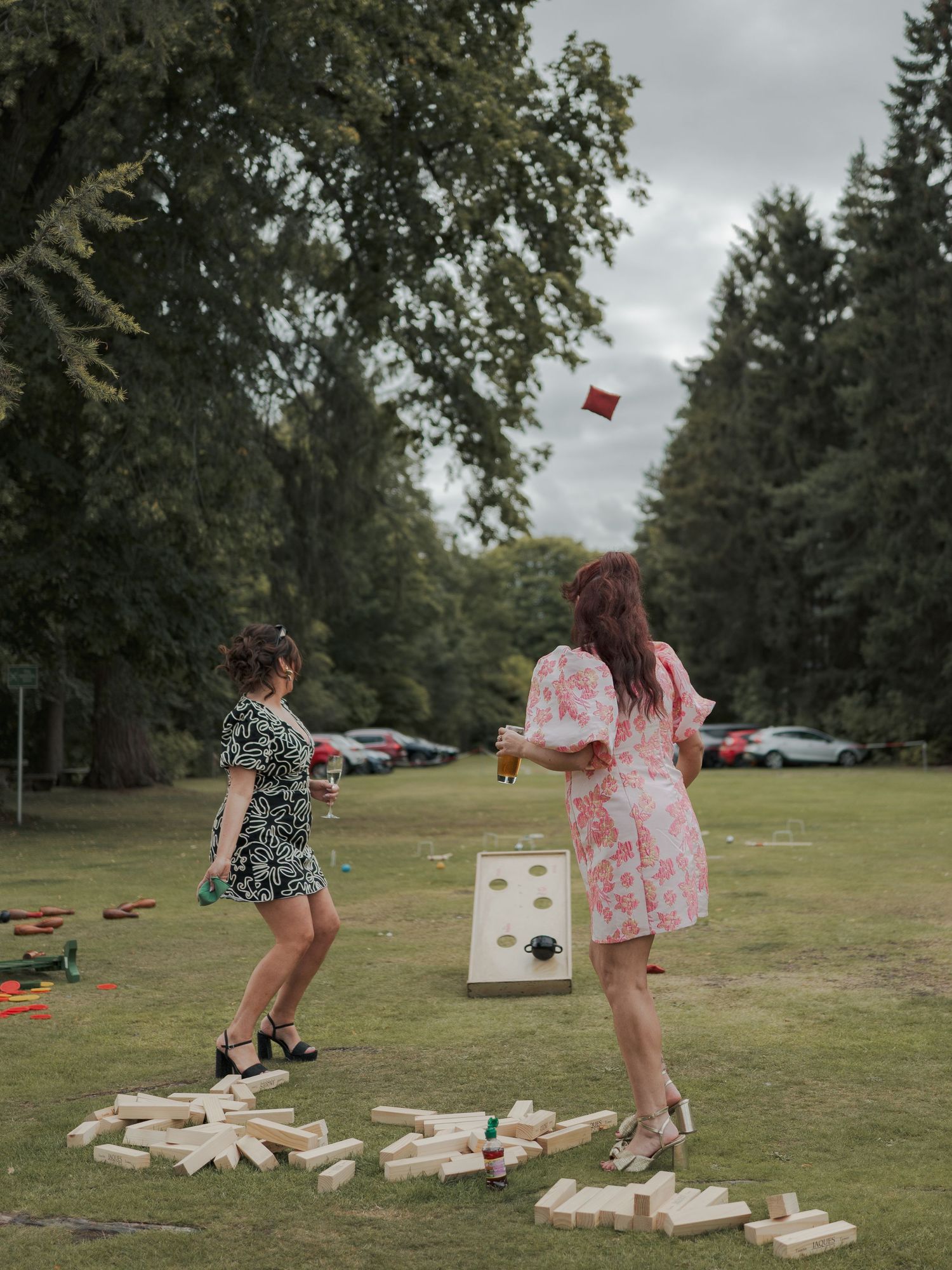 Two people playing the giant yard game Jenga in a grassy area with scattered blocks at their feet.
