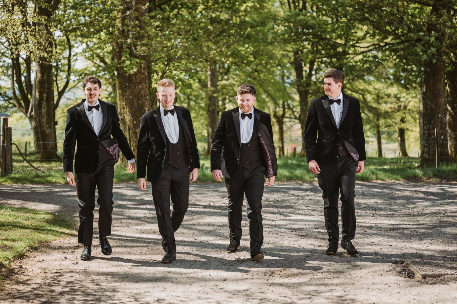 Groom and groomsmen in black tuxedos walk together on a tree-lined path during a wedding at Kinclune House.