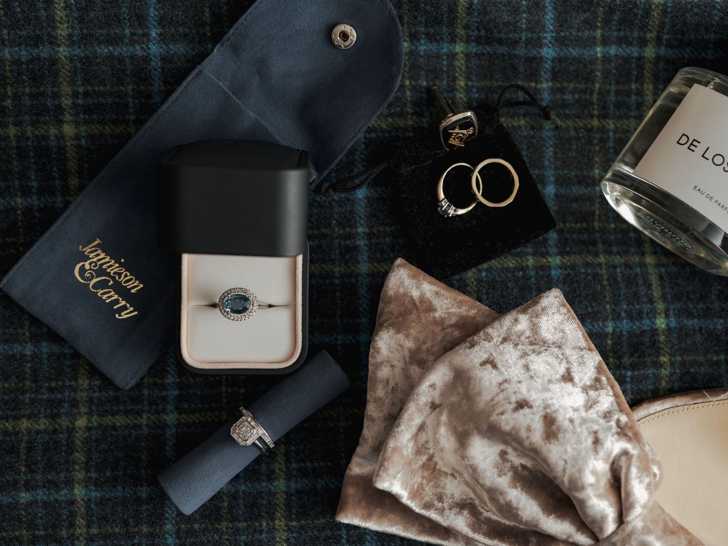 A collection of wedding rings and jewelry displayed on a dark plaid fabric with scattered decorative elements.