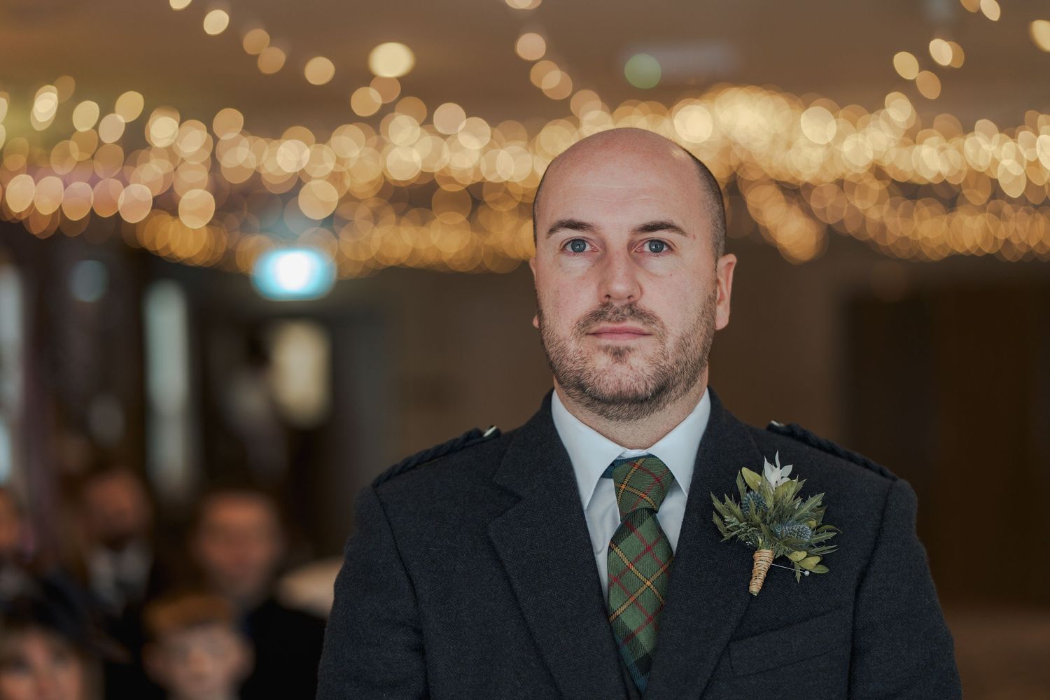 Groom in Scottish highland dress with thistle boutonniere stands at wedding ceremony altar.