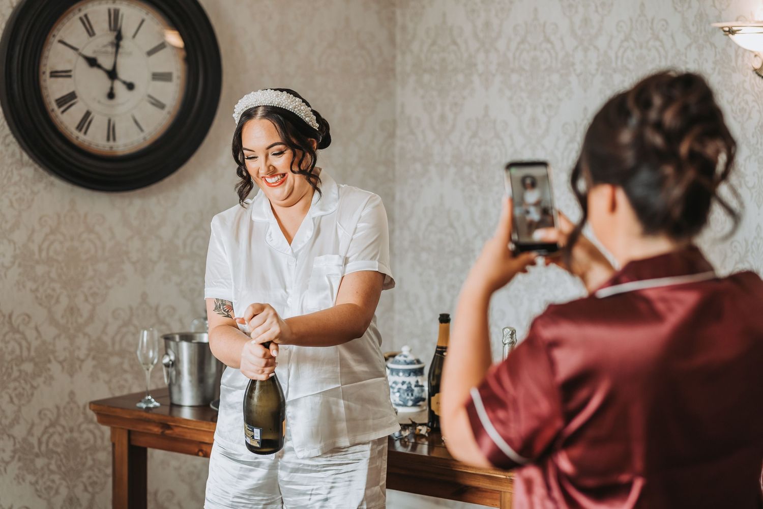 A photographer captures a moment in a vintage-style kitchen setting with a clock on the wall and bottles on wooden table.