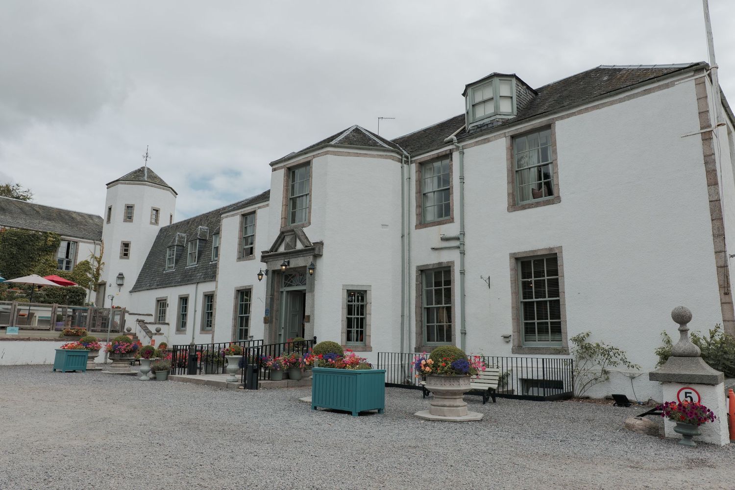 Elegant white historic building with dormer windows and outdoor seating area in front on a cloudy day at Banchory Lodge.