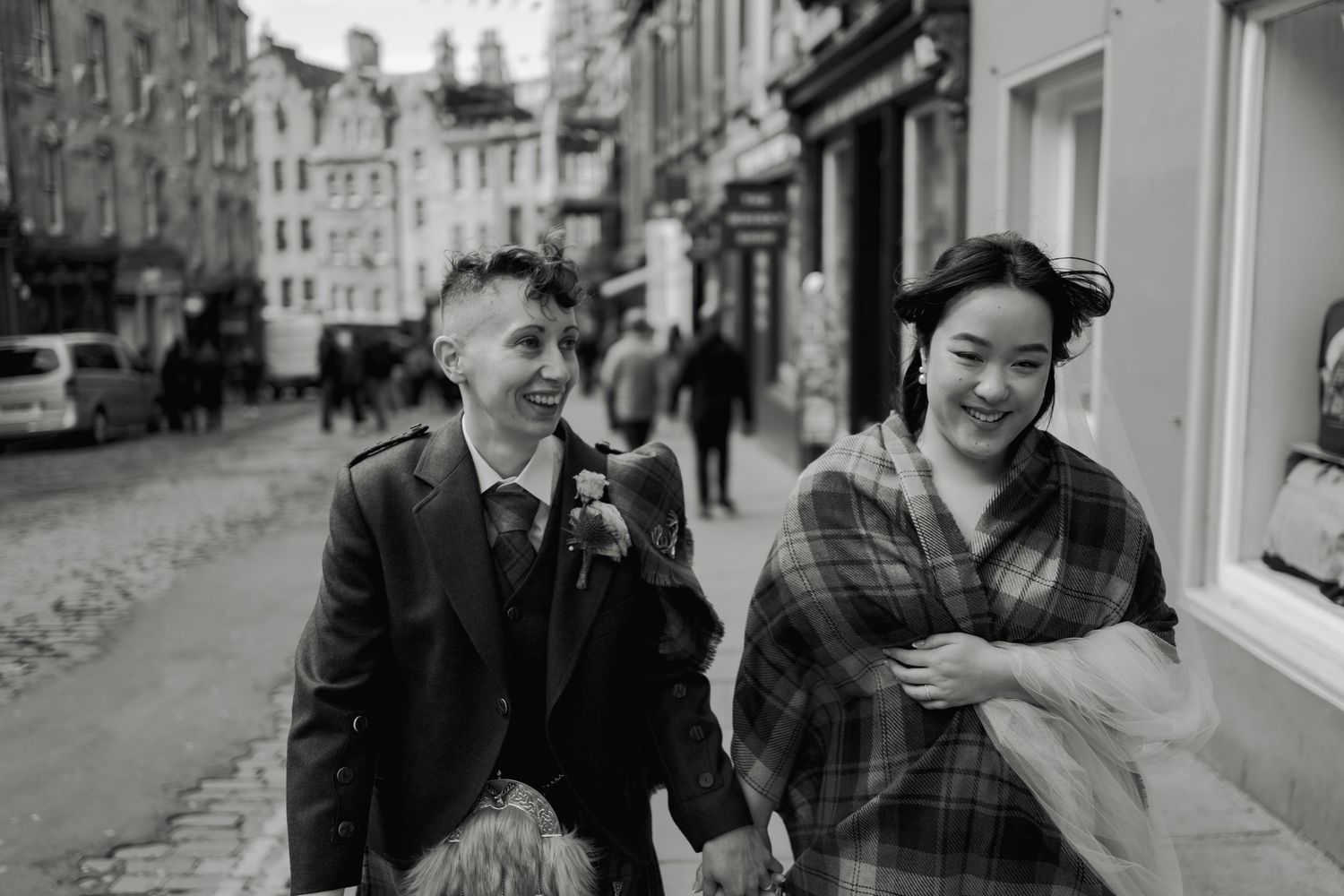 Black and white photo of two brides laughing on Victoria Street in Edinburgh on their wedding day.