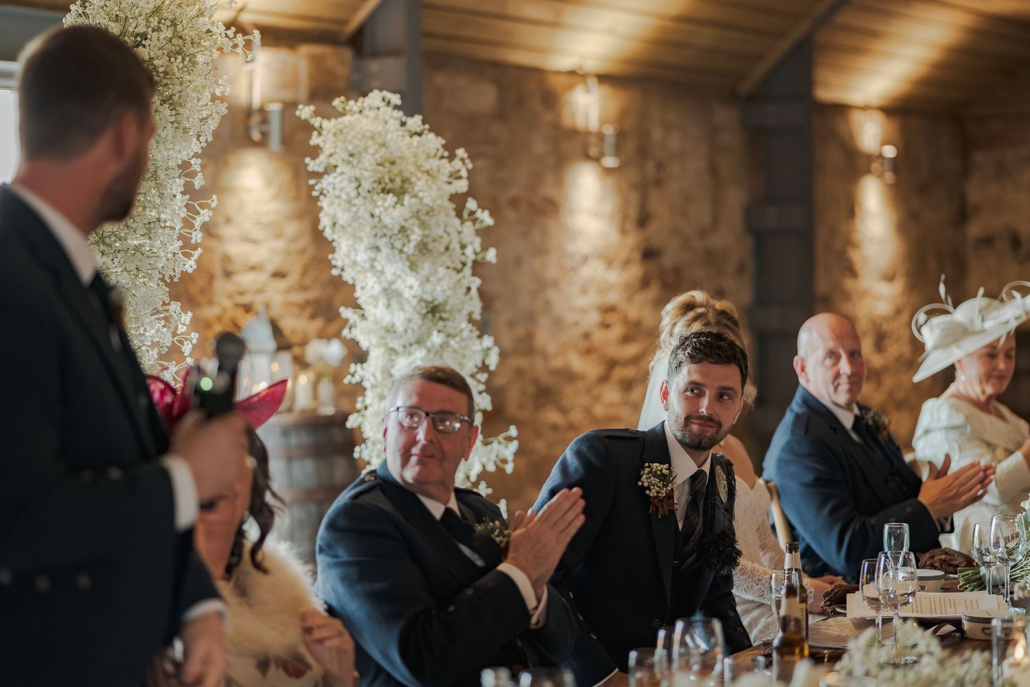 Wedding guests share laughter and conversation during an elegant reception at Falside Mill with floral decor.