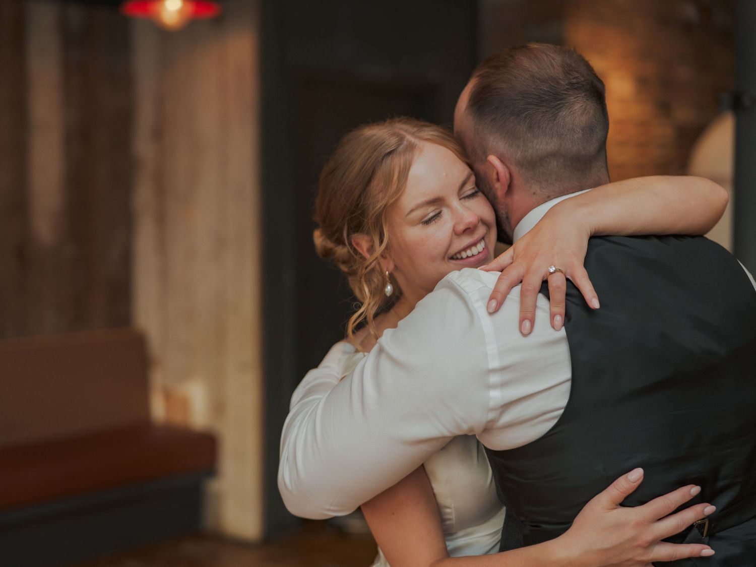 A couple shares a tender embrace during a wedding ceremony in a rustic venue with warm lighting.