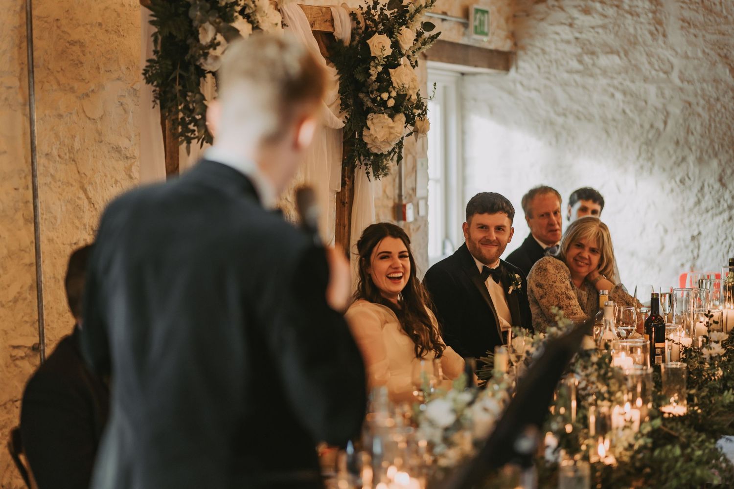 Wedding guests react with smiles and laughter to a candlelit reception speech in the intimate stone-walled venue Kinclune House.