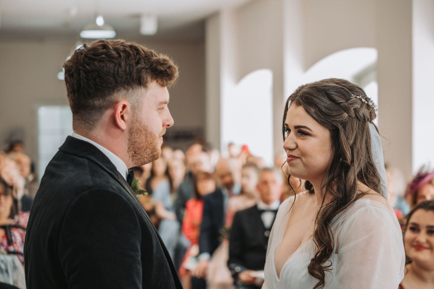 Two people share a meaningful moment during their wedding ceremony at Kinclune House while guests look on from the background.