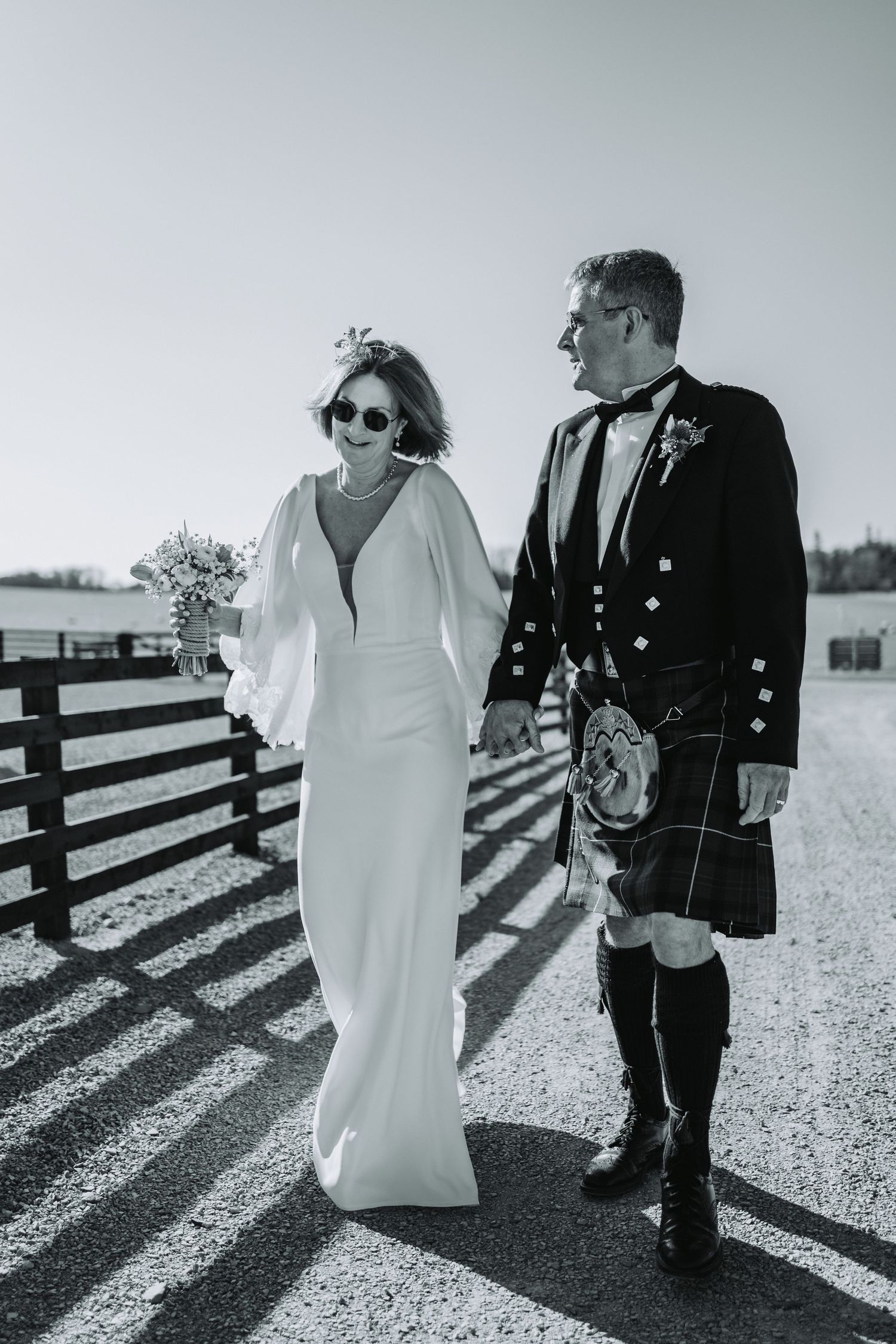 Black and white portrait of couple walking together at Falside Mill, featuring Scottish wedding attire.