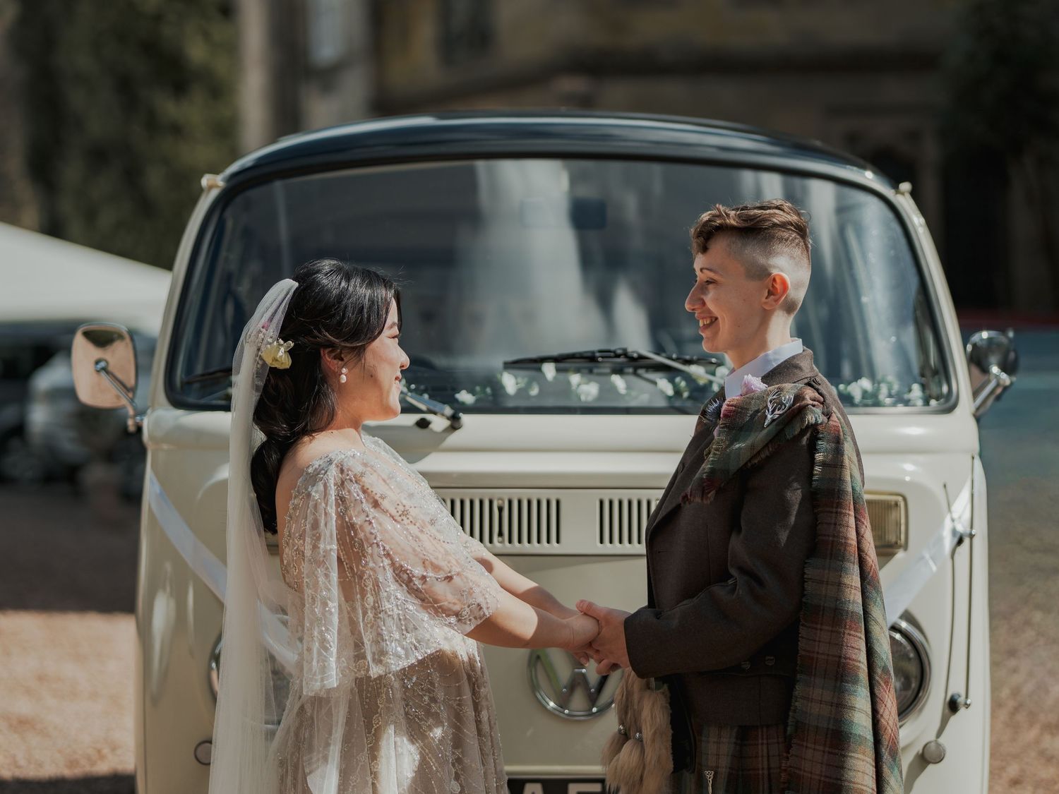 Bride and groom holding hands in front of a vintage cream VW camper van decorated with white ribbons at Melville Castle