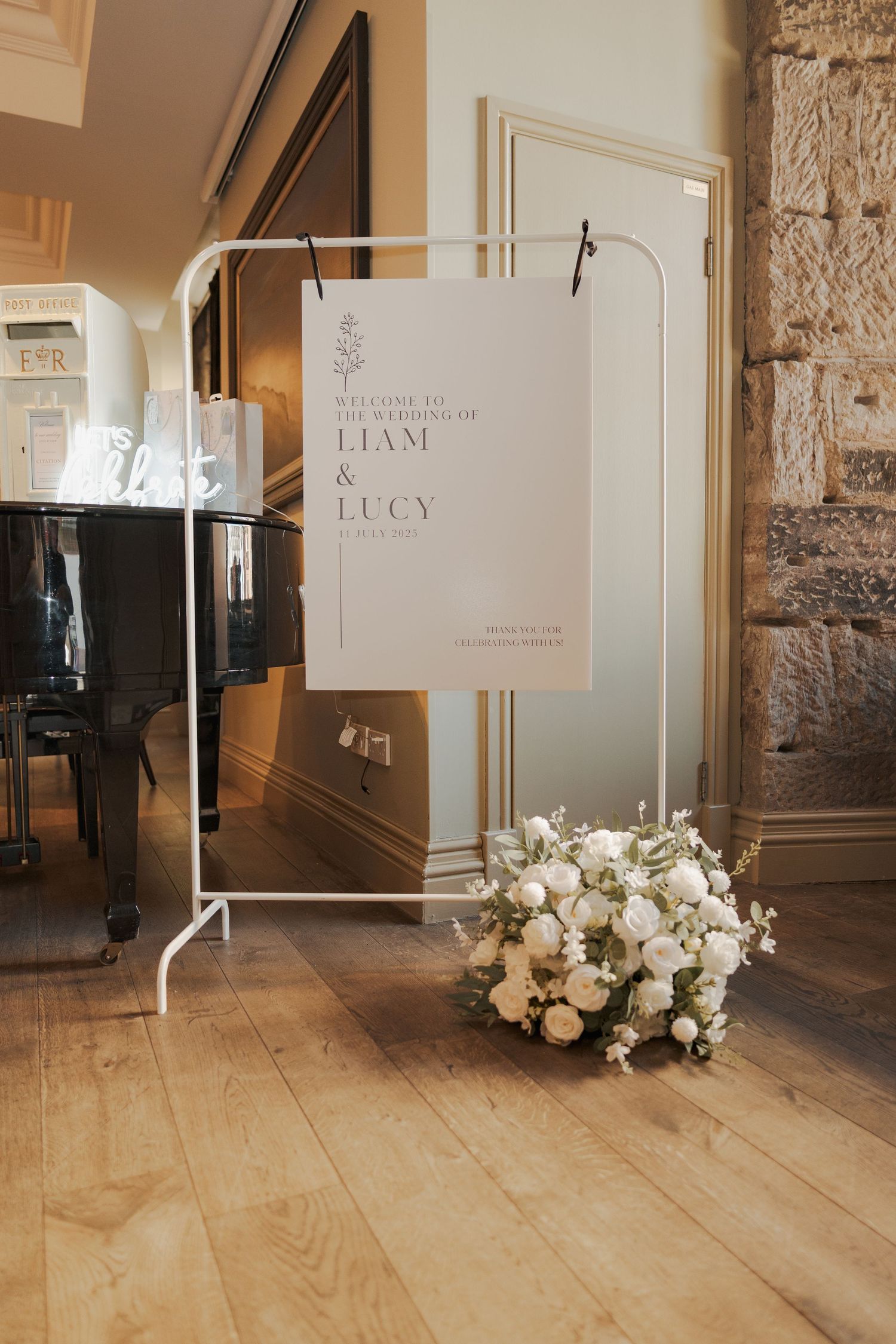 Elegant wedding signage and white floral arrangements displayed along a light wooden floor in a rustic venue.