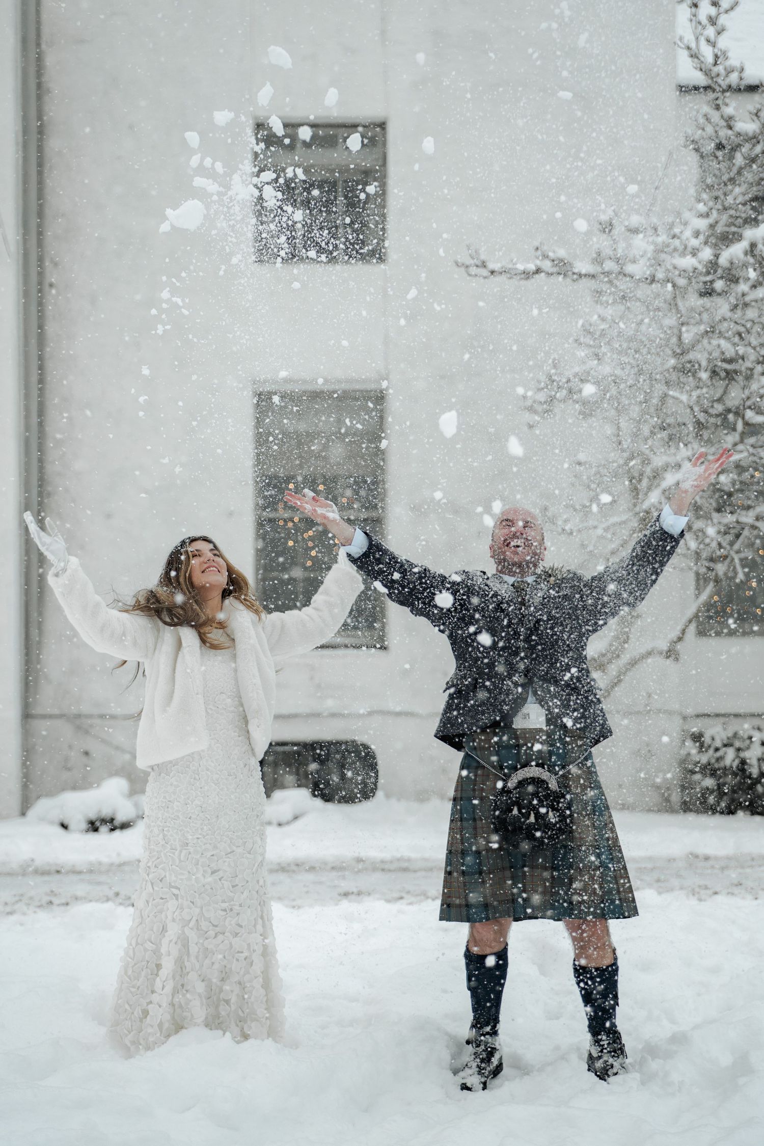 Bride and groom tossing snow in the air during a winter wedding, man wearing a traditional Scottish kilt.
