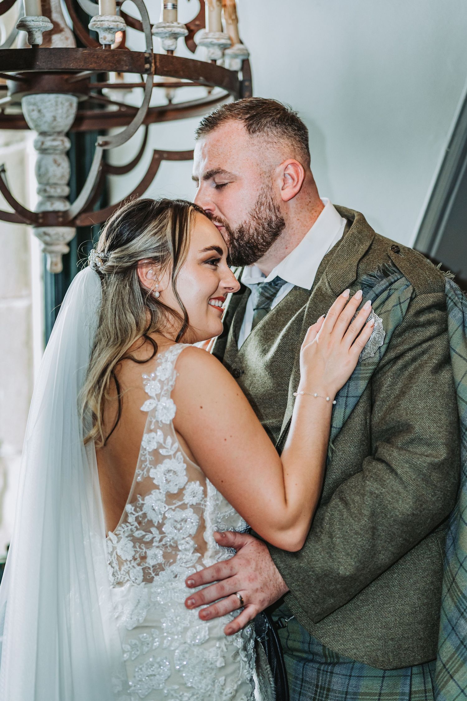 Intimate moment between newlyweds sharing a tender embrace under a vintage chandelier at Cornhill Castle.