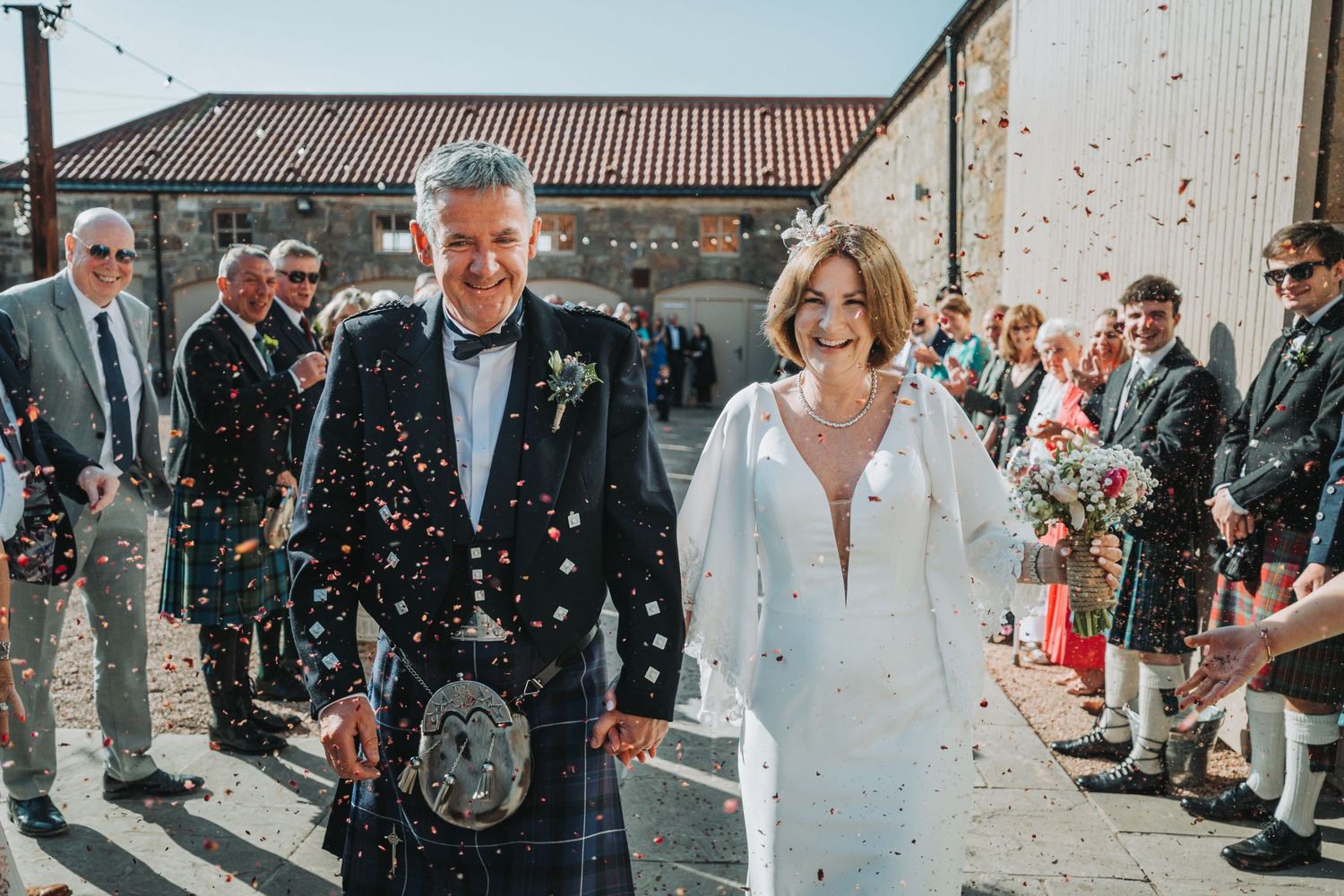 Newlyweds walk through confetti shower at Falside Mill while guests celebrate their Scottish wedding ceremony.