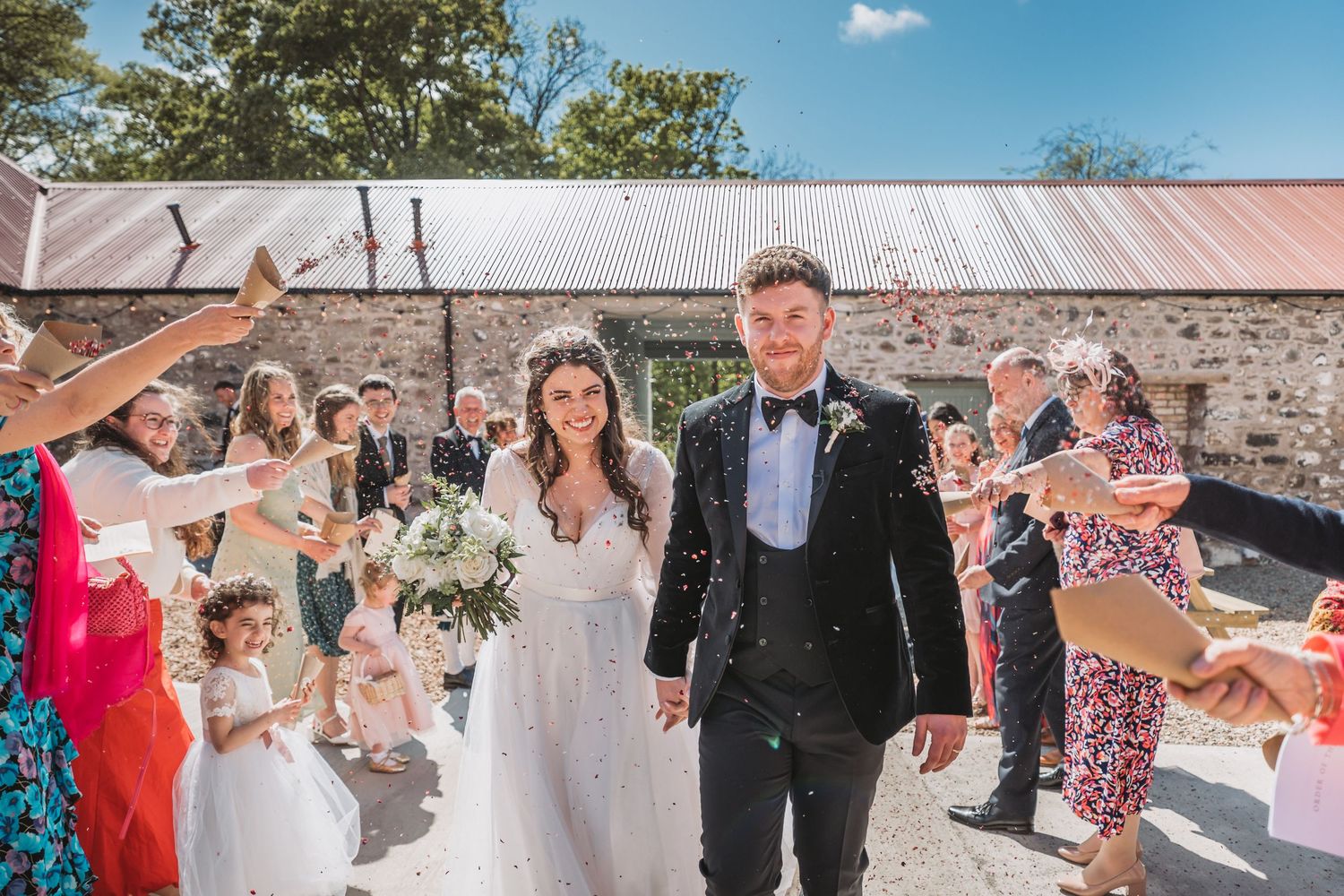 Wedding guests throw confetti as a couple walks down a path at Kinclune Steading.