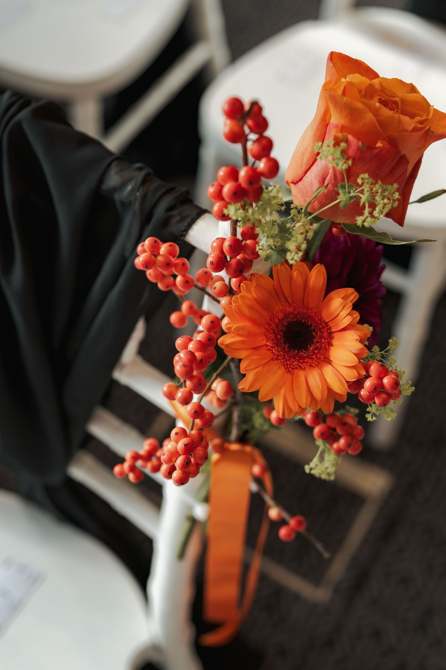 Orange gerbera daisy and red berries arranged in decorative vases create elegant wedding centerpieces.