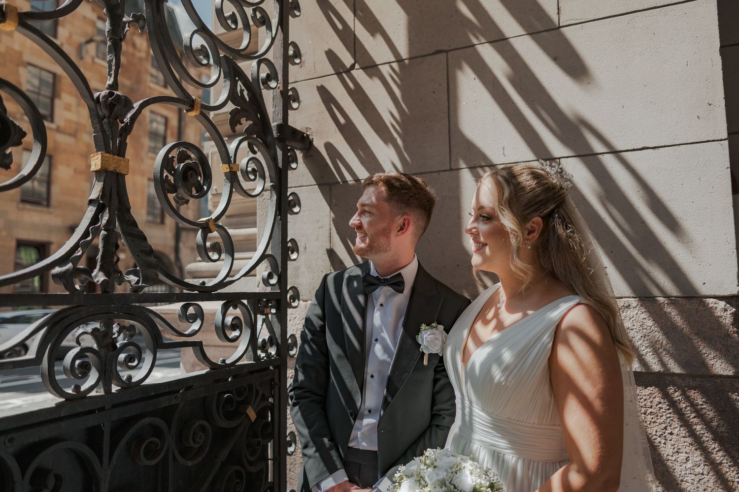 Couple sharing an intimate moment on an elegant staircase with ornate black iron railings and natural light streaming in.