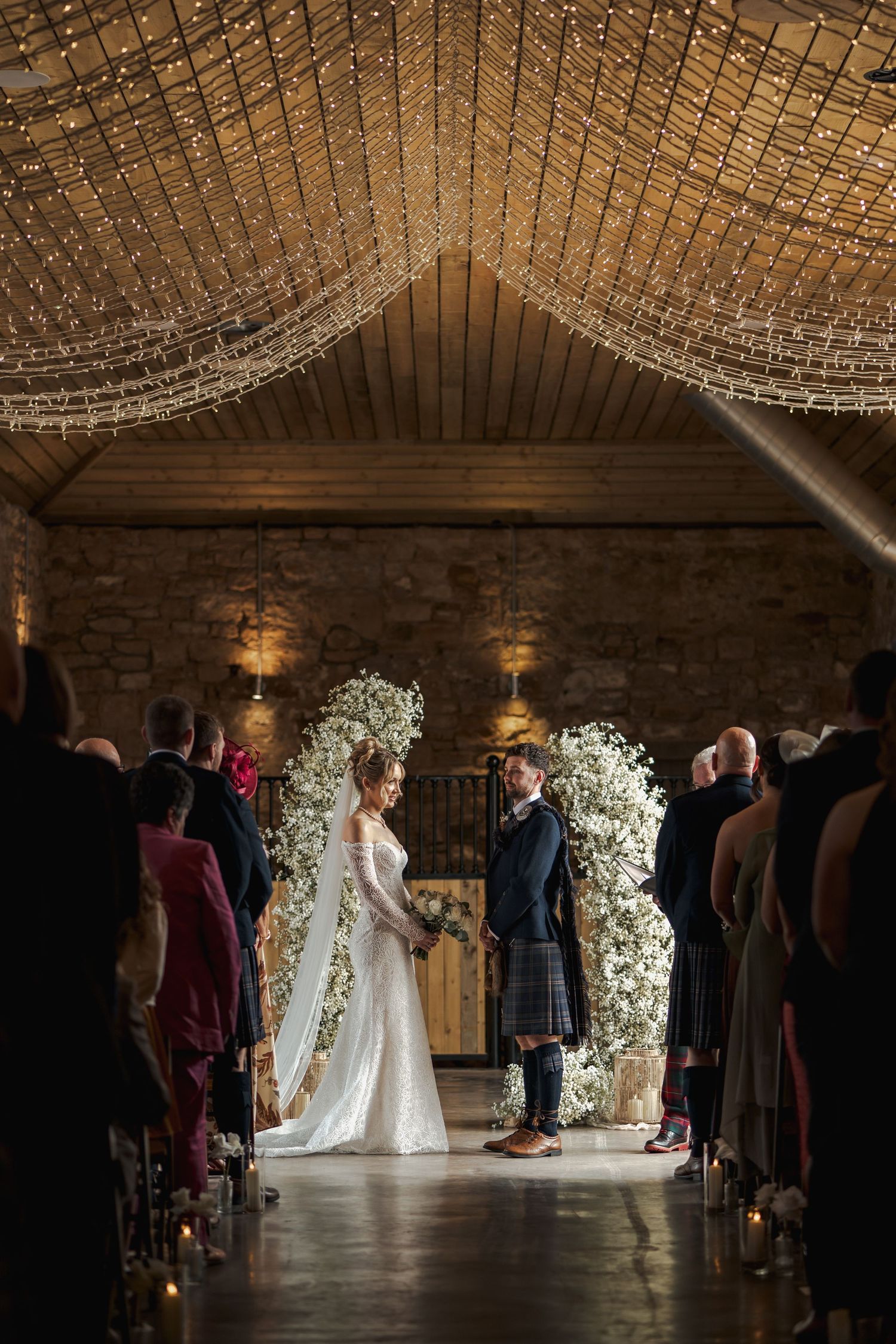 Wedding ceremony at Falside Mill with floral arch and guests watching from both sides.