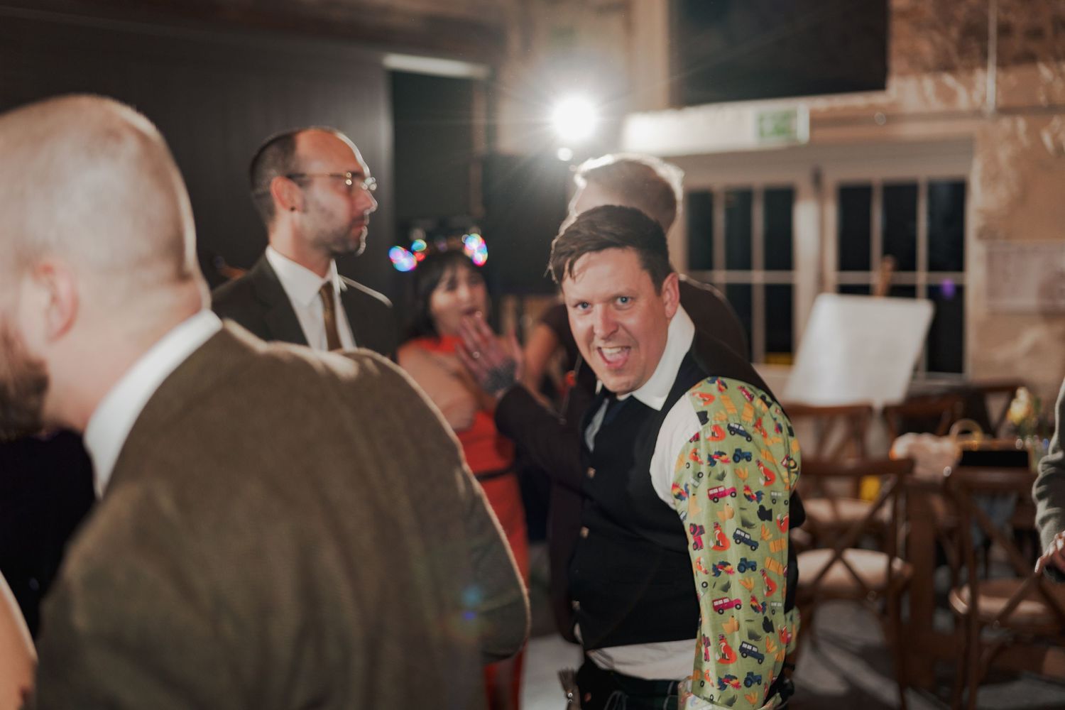 Man in colorful floral jacket socializing with guests at an elegant indoor wedding reception.