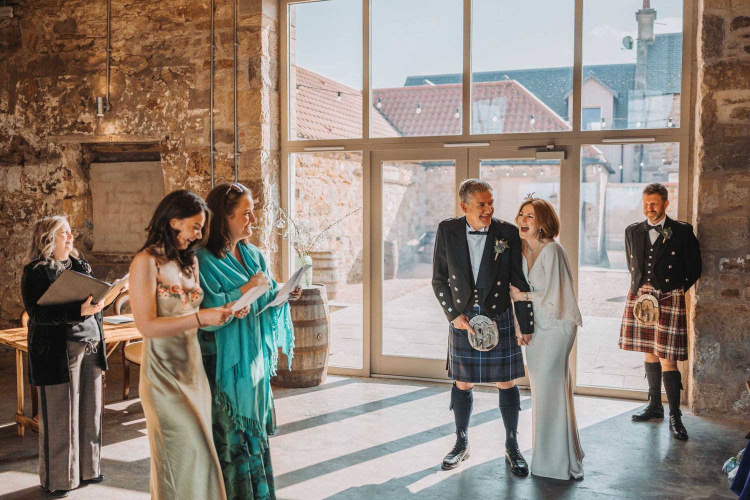 Wedding party in mix of traditional Scottish and formal wear gathering in sunlit Falside Mill.