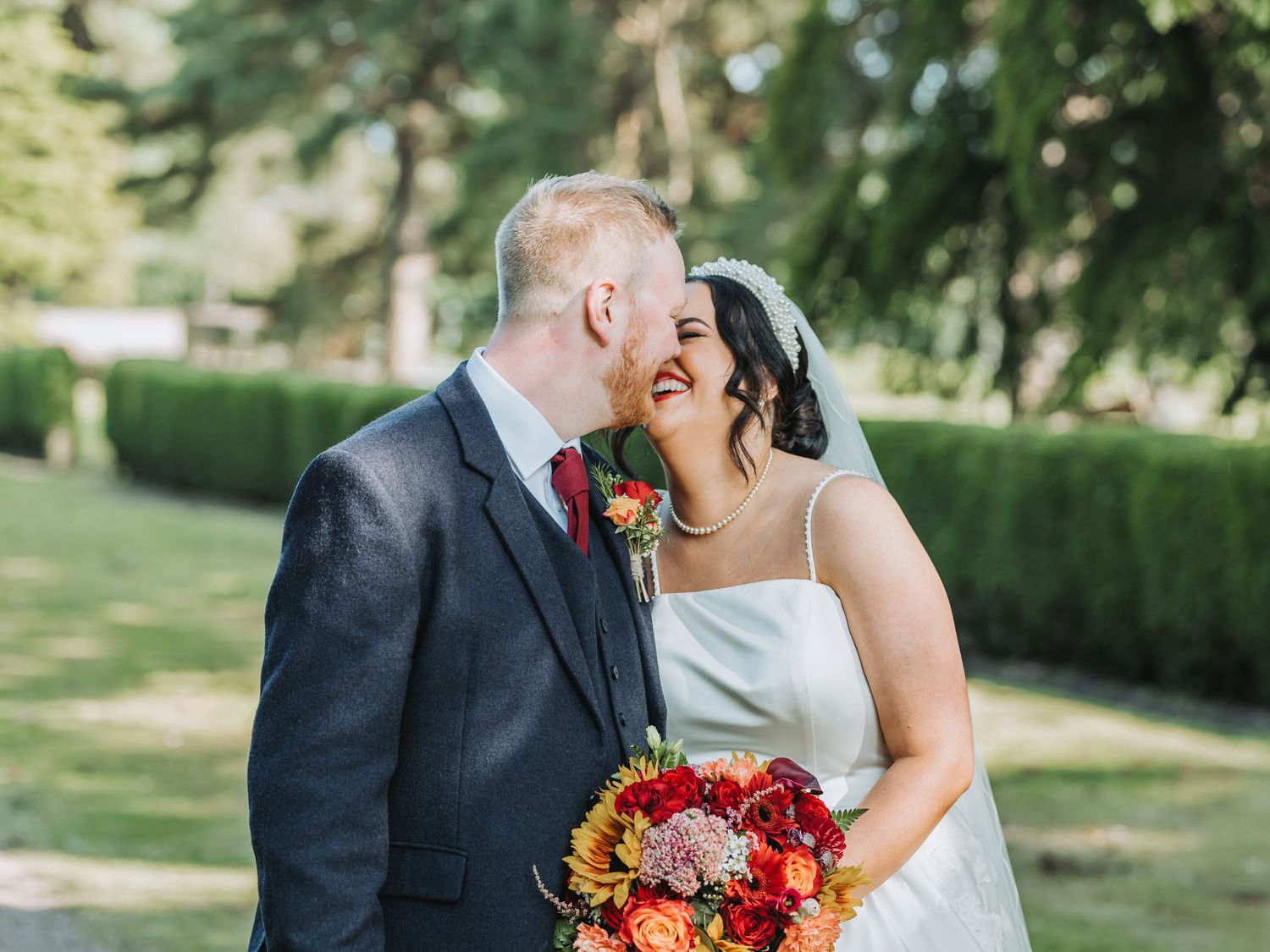 Happy wedding couple share intimate moment outdoors at Oswald House holding vibrant autumn bouquet of sunflowers.