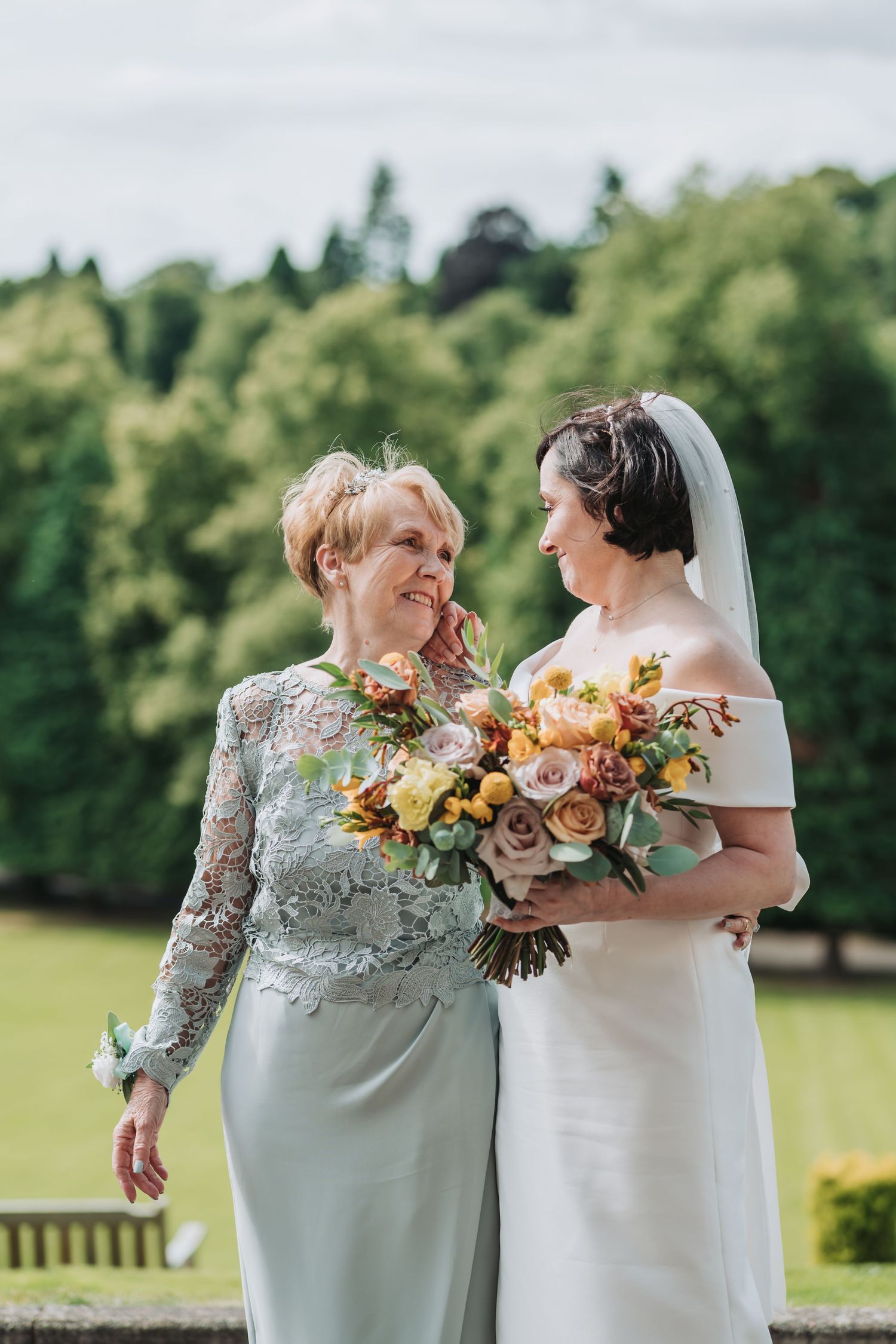 Two people in elegant formal wear share a joyful moment outdoors at Dunblane Hydro while holding a beautiful autumn-toned bouquet.