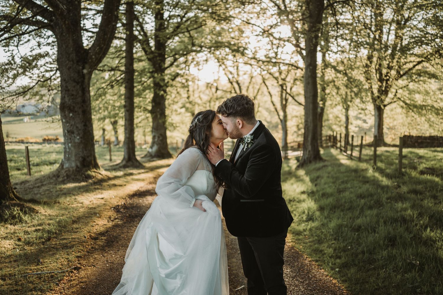 Newlyweds embrace in romantic sunset moment along tree-lined path during outdoor wedding photoshoot at Kinclune House.