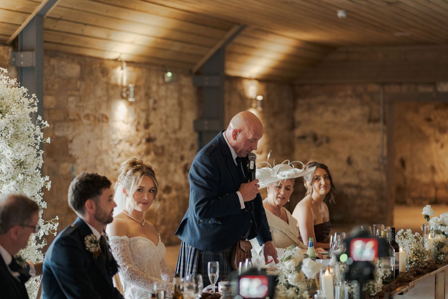 Wedding guests sharing emotional moments during reception in rustic brick venue with soft lighting and floral decorations.