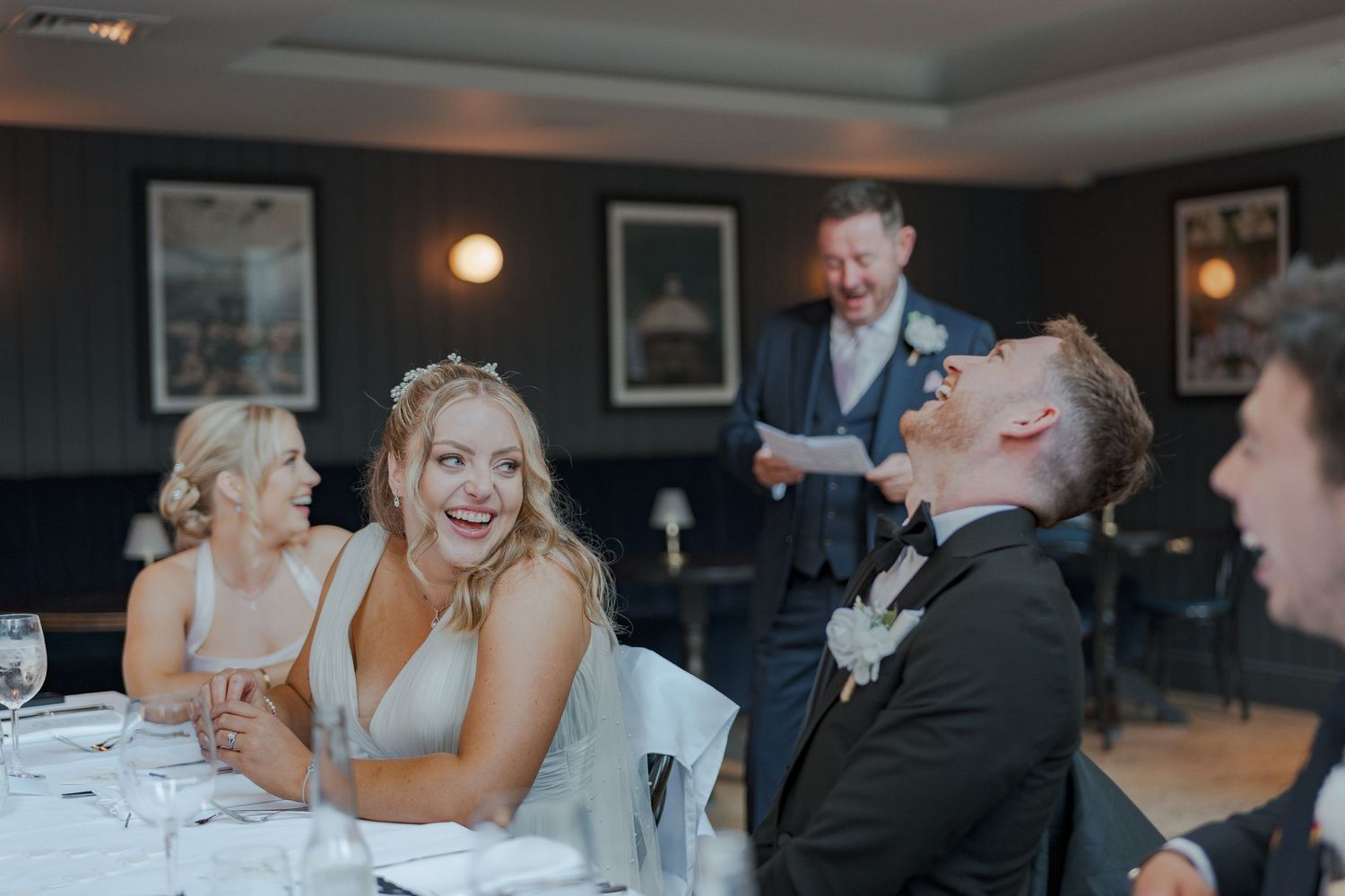 Guests share a joyful moment of laughter during a wedding reception at an elegant indoor venue.