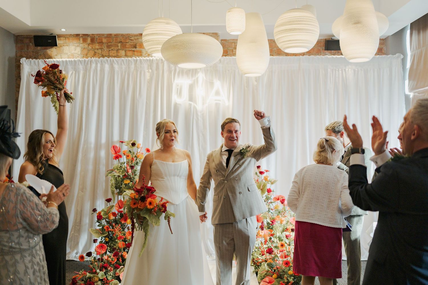 A wedding celebration with floral arrangements and paper lanterns decorating an indoor venue.