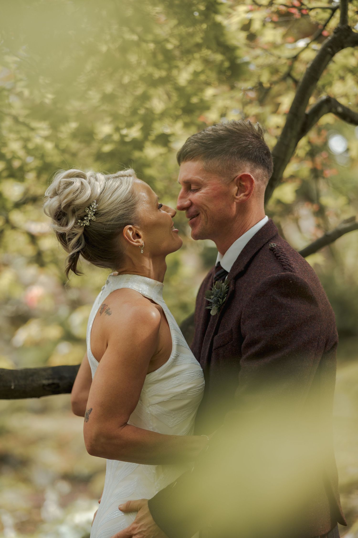 A bride and groom share a romantic moment outdoors, surrounded by lush green foliage on their wedding day.
