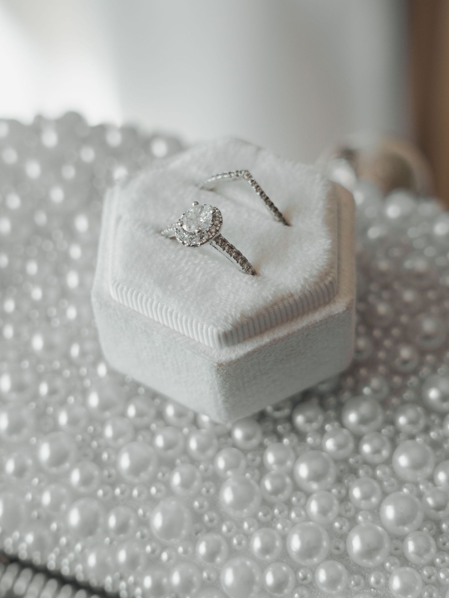 Wedding rings displayed on white heart-shaped cushions surrounded by delicate white pearl beads in a romantic arrangement.
