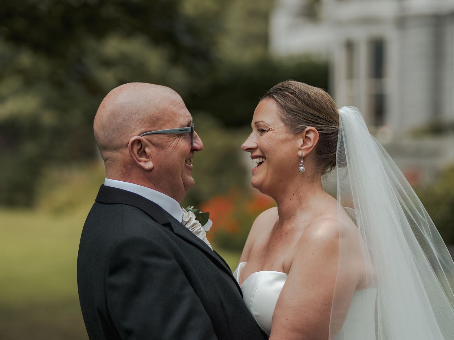Smiling bride and groom share a joyful moment outdoors, with the bride in a white gown and veil on their wedding day.