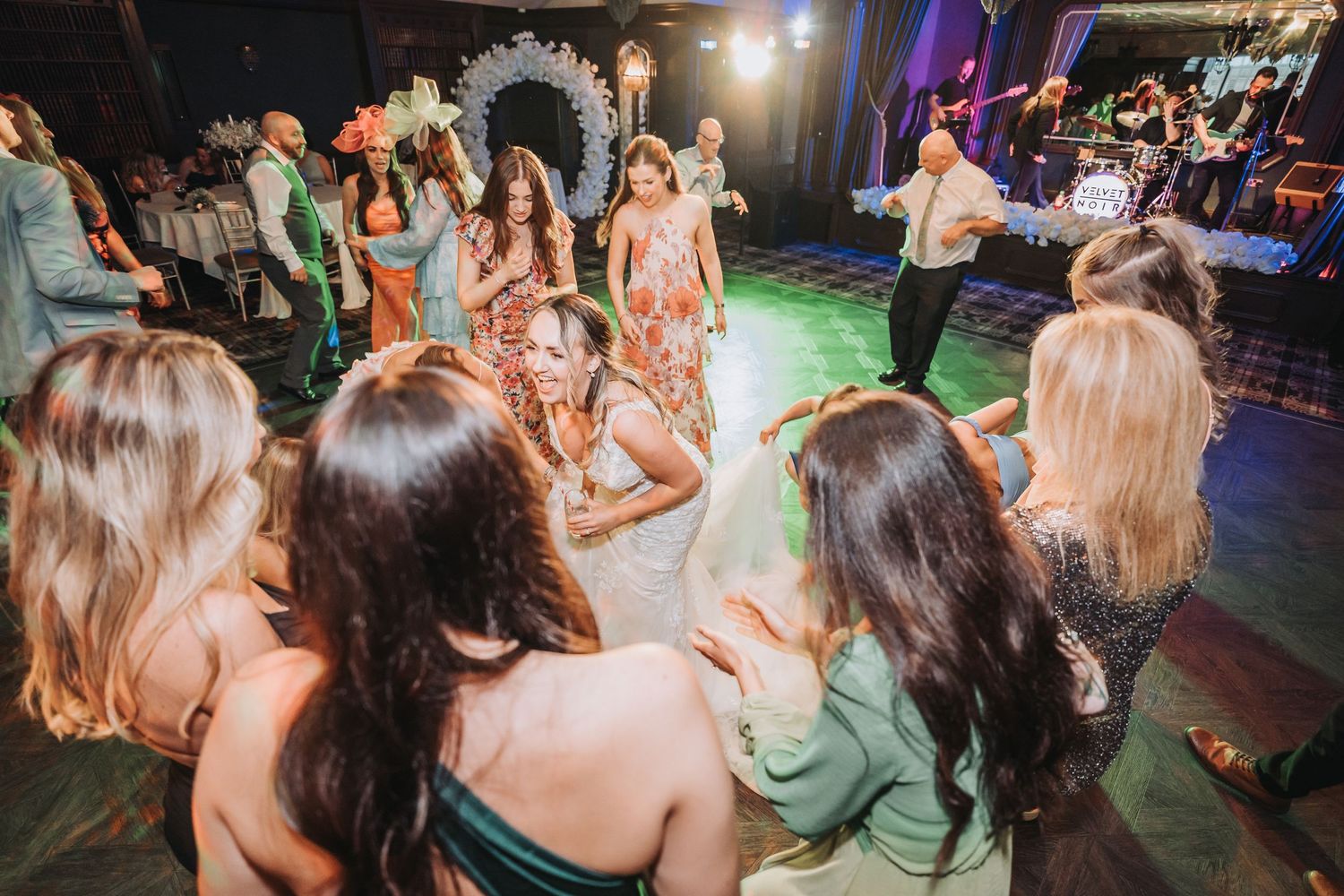 Wedding reception guests dancing together on a vibrant dance floor under bright lights at a festive celebration.