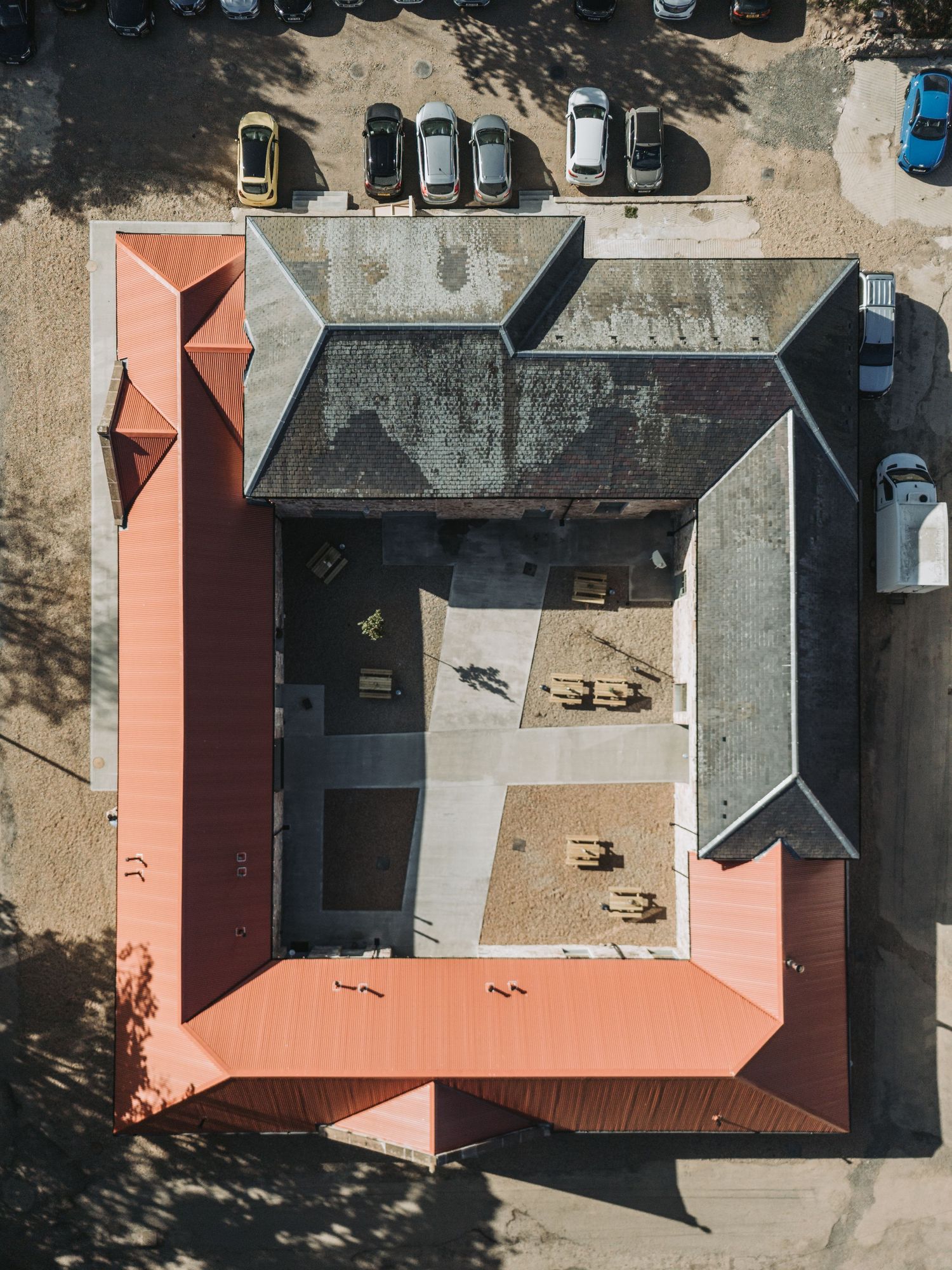 Aerial drone view of Kinclune Steading, with red terracotta roof and parked cars surrounding it in a parking lot.