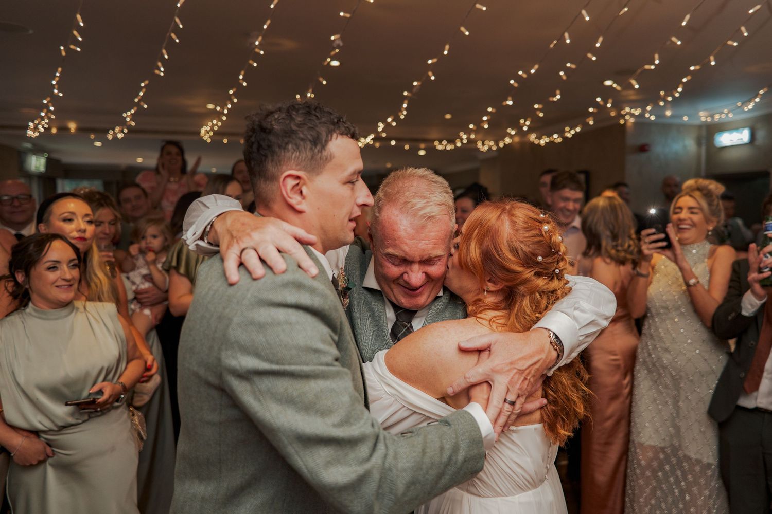 Groups of couples dancing and embracing on a dimly lit dance floor with string lights overhead during a celebration at Banchory Lodge.