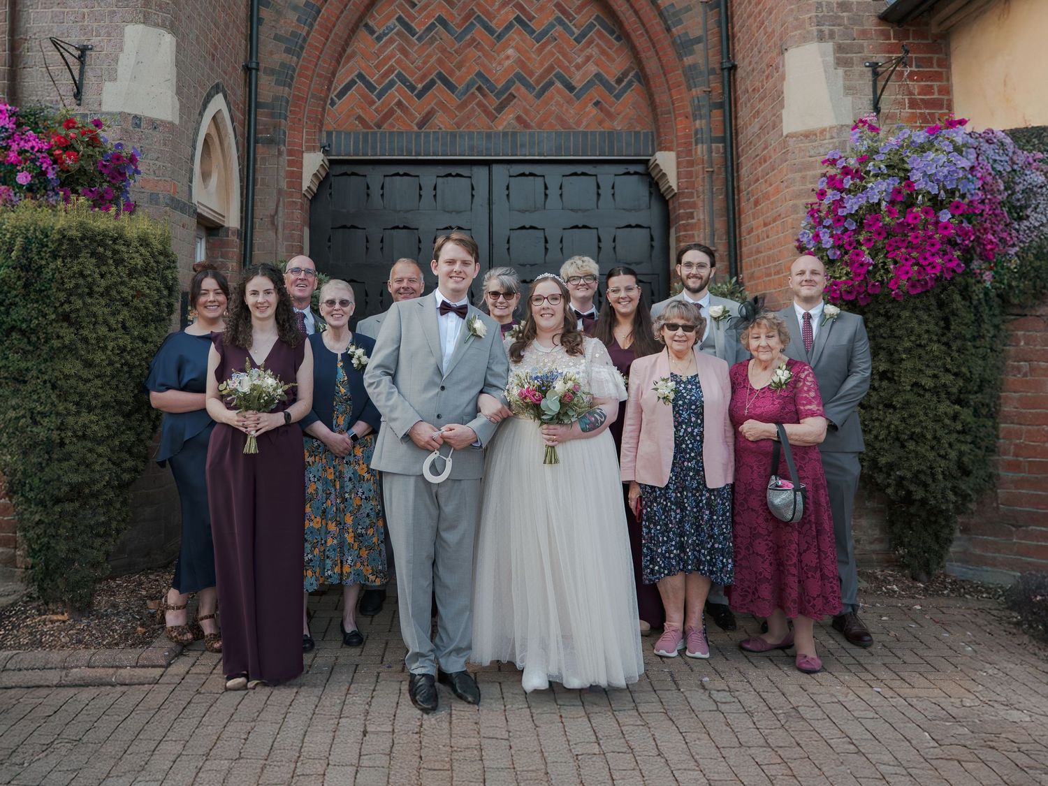 A series of wedding party group photos taken outside a brick church with colorful flowers and ornate doors.