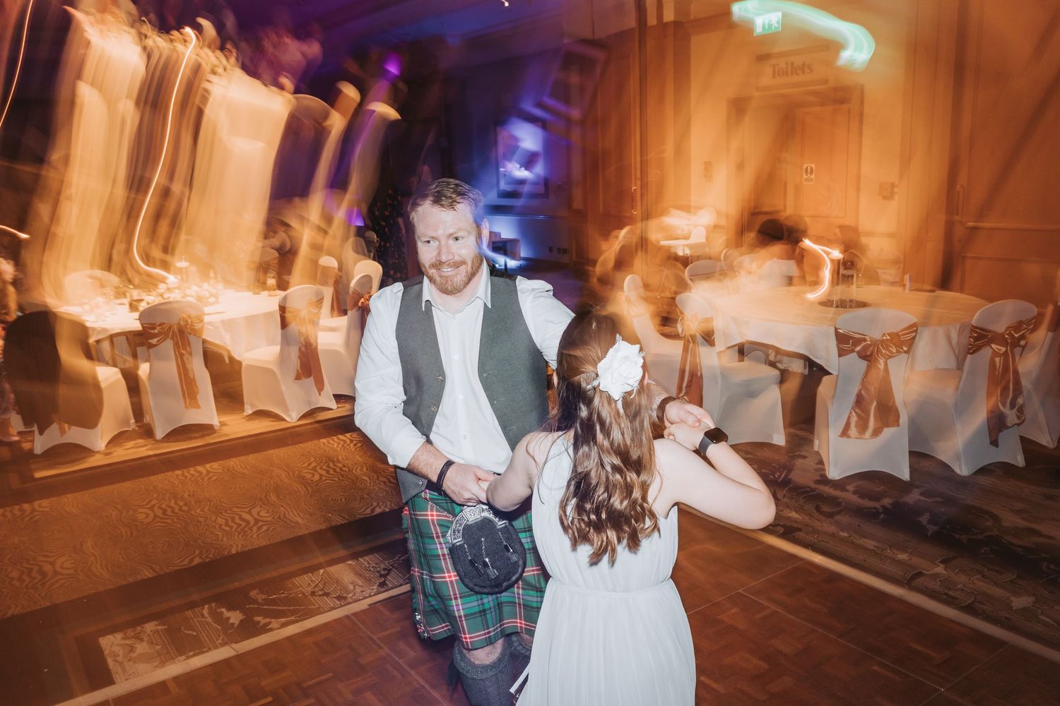 Dancing couple celebrates with motion blur on wedding reception dance floor in warm lighting effect.