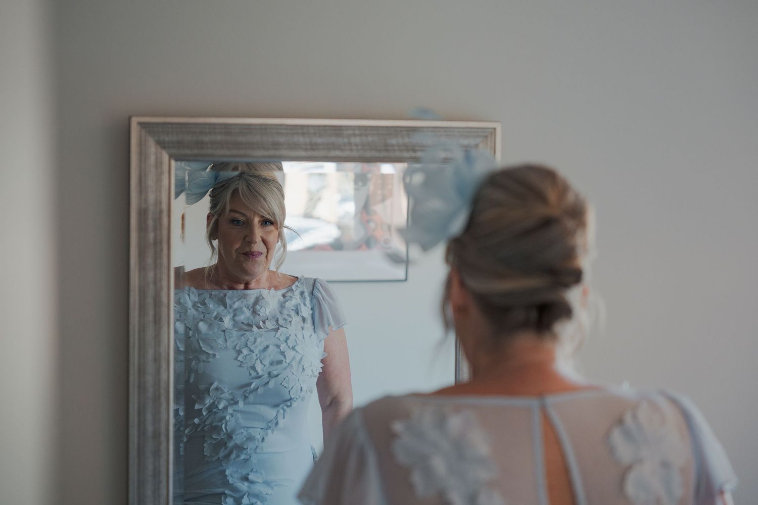 Person in a floral dress adjusts their hair in a mirrored reflection while standing in a room.