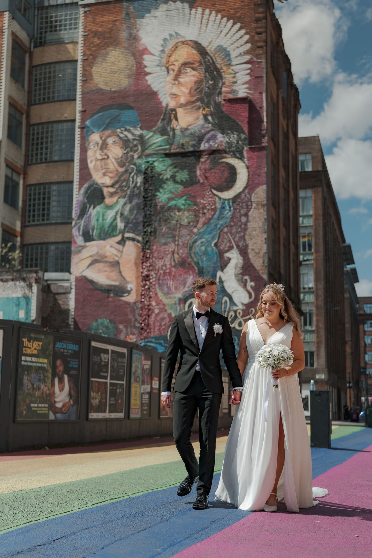 Newlywed couple poses for wedding photos in front of vibrant street art murals on a sunny day.