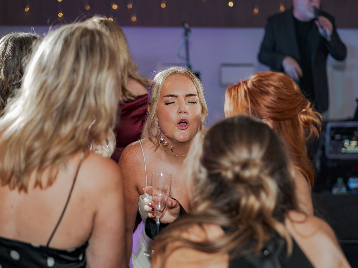 A group of people dancing and celebrating at a party with festive lighting in the background.